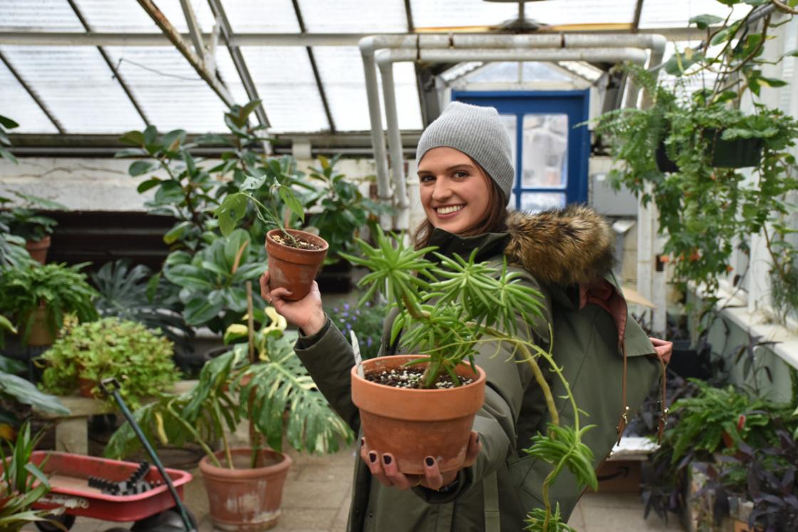 Photograph of a smiling woman holding plants in the Conservatory Greenhouse.
