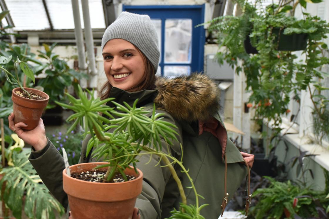 Photograph of a smiling lady holding a plant in the Conservatory Greenhouse.